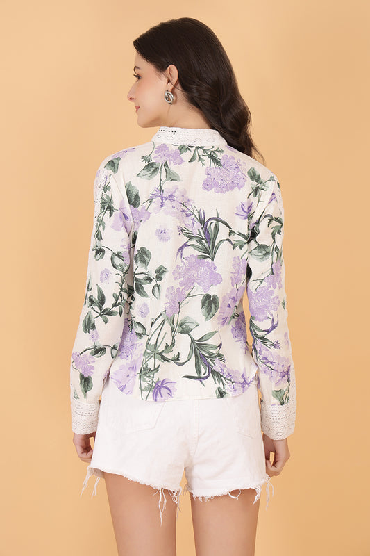 Woman wearing a floral linen shirt and white shorts against a beige background